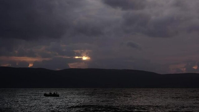 Empty boat swaying by the wind in the sea. Golden sunset above a mountain range. Magnificent nature landscape with tropical storm clouds and warm lights. Last rays of the sun on a windy evening.