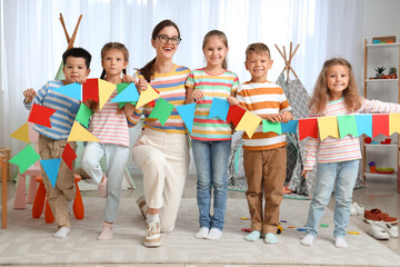 Little children with nursery teacher and paper flags in kindergarten