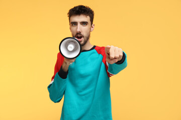 Young man with megaphone pointing at viewer on yellow background, closeup