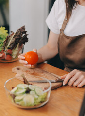 Delicious fruit and vegetables on a table and woman cooking. Housewife is cutting green cucumbers on a wooden board for making fresh salad in the kitchen.