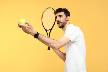Young man with tennis racket and ball on yellow background