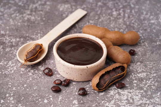 Bowl with tasty tamarind jam and fruits on grey background