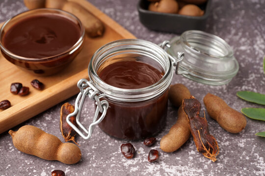 Jar and bowl of tasty tamarind jam with fruits on grey background