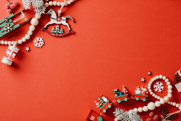 Retro style Christmas flat lay composition with wooden garland, decorations, toys on red background.
