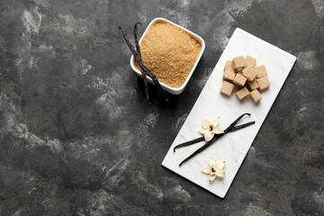 Board and bowl of aromatic vanilla sugar, flowers with sticks on black background