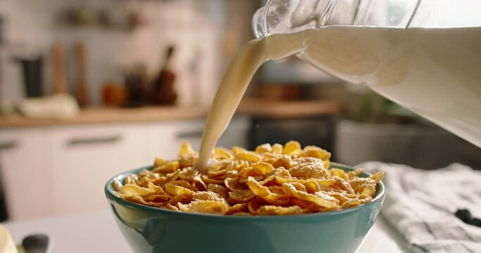 Unknown pours milk over breakfast cereal at beautifully decorated table modern kitchen. Advertising cinematic slow motion. Beautiful calm dream breakfast on cozy sunny morning. Healthy nutrition food