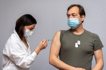 A military man wearing a medical mask is vaccinated in the arm by a doctor, vaccination in the army and preventive measures. - obrazy, fototapety, plakaty