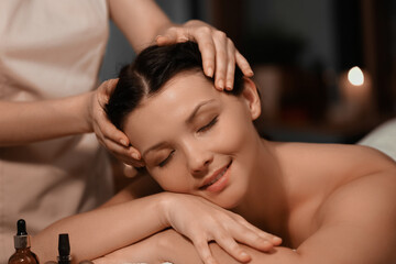 Beautiful young woman getting facial massage in dark spa salon, closeup