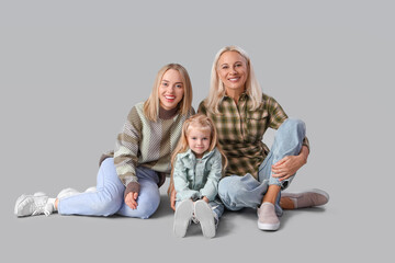 Cute little girl with her mother and granny sitting on light background