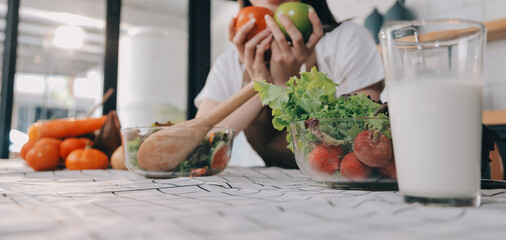 Delicious fruit and vegetables on a table and woman cooking. Housewife is cutting green cucumbers on a wooden board for making fresh salad in the kitchen.