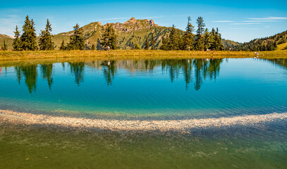 Alpine summer view with reflections and hikers at Lake Spiegelsee, Mount Fulseck, Dorfgastein, St....