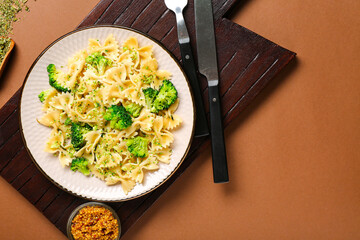 Plate of tasty pasta with broccoli on brown background