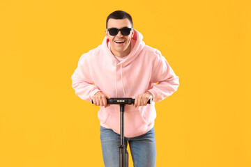 Fototapeta na wymiar Cool young man riding electric scooter on yellow background