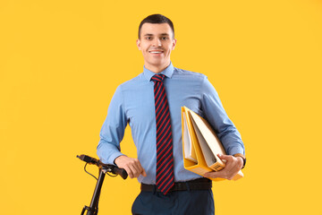 Young businessman with folders and electric scooter on yellow background