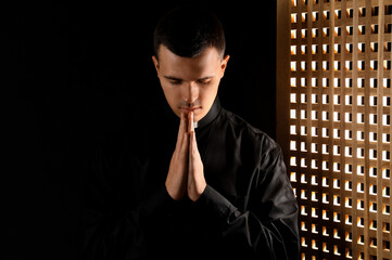 Young priest praying in confession booth