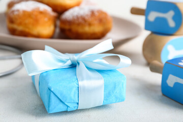 Gift box, dreidels and donuts for Hanukkah celebration on light background, closeup