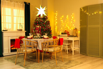 Interior of festive room with Christmas tree, decorations, fireplace and served dining table at evening