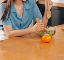 A young woman with a beautiful face in a blue shirt with long hair eating fruit sitting inside the kitchen at home with a laptop and notebook for relaxation, Concept Vacation.