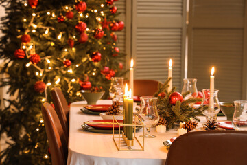 Festive table setting with Christmas decorations and burning candles in dining room