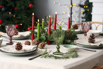 Festive table setting with Christmas decorations, burning candles and pine cones in dining room, closeup