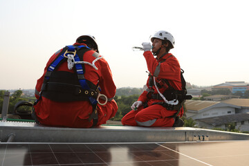 Two male Solar engineers with Red Safety Hazard dress  and wearing safety hardness resting during...