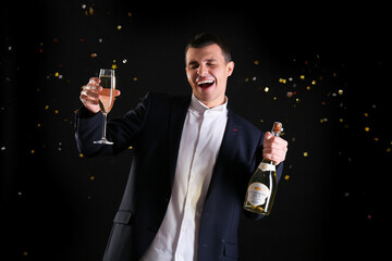 Happy young man with bottle and glass of champagne celebrating Christmas on black background