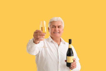 Senior man with glass and bottle of champagne celebrating Christmas on orange background