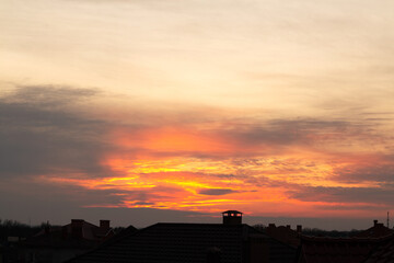 Roofs of houses against the backdrop of a beautiful sunset. Scenic view of orange sky with clouds during sunset.