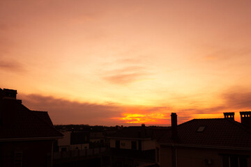 Scenic view of orange sky with clouds during sunset. Roofs of houses against the backdrop of a beautiful sunset.