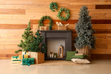 Fireplace with small Christmas trees, gift boxes and wreathes near wooden wall