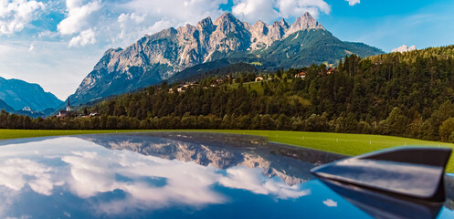High resolution stitched alpine summer panorama with reflections on a car roof, a church and the...
