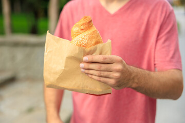 Guy's hand holds a croissant, snack and fast food concept. Selective focus on hands with blurred...