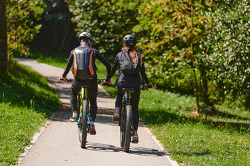 Fototapeta premium A blissful couple, adorned in professional cycling gear, enjoys a romantic bicycle ride through a park, surrounded by modern natural attractions, radiating love and happiness