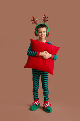 Cute little boy in reindeer horns with pillow on brown background
