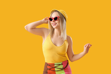 Pretty young woman in retro outfit and sunglasses on yellow background