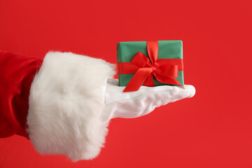 Santa hand with gift box on color background, closeup