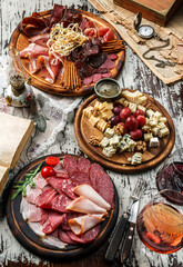 Snacks and Wine appetizer sets, cold meat plates with sausage, ham, salami, prosciutto, bacon and cheese plate with parmesan, blue cheese, brie cheese, cheddar on wooden background with glass of wine