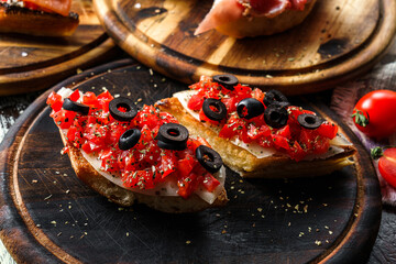 Bruschetta with fish, bell pepper, cream cheese and olives on ciabatta bread on wooden board over...
