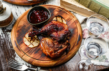 Grilled duck legs and bbq chicken meat with sauce, apples on wooden background with glasses of vodka. Holiday food, top view