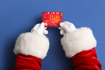 Santa hands with gift card on blue background, closeup