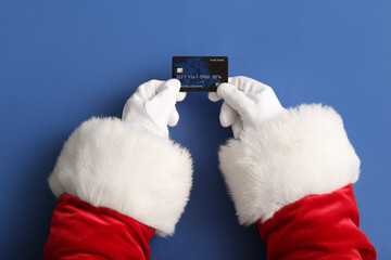Santa hands with credit card on blue background, closeup