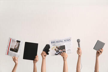 Female hands with newspapers, microphones and notebooks on light background