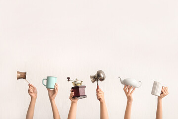 Female hands with coffee grinder, jezve, teapot and cups on light background