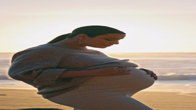 Expectant mother posing sunset beach caressing belly vertical. Pregnant woman