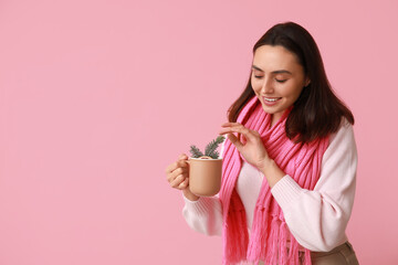 Beautiful young woman in scarf with cup of hot mulled wine on pink background