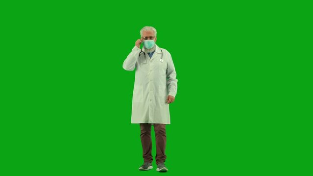 Portrait of aged man medic on chroma key green screen. Senior doctor in uniform walking in medical mask, taking it off and fixing his outfit.