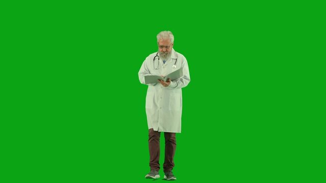 Portrait of aged man medic on chroma key green screen. Senior doctor in uniform walking holding reading papers with analysis and diagnosis.