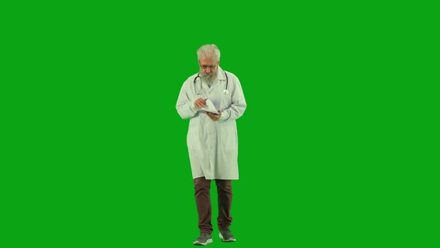Portrait of aged man medic on chroma key green screen. Senior doctor in uniform walking holding reading medical card with history of diagnosis.