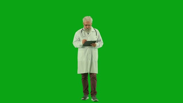 Portrait of aged man medic on chroma key green screen. Senior doctor in uniform walking holding clipboard and writing notes on paper.