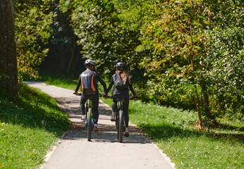 A blissful couple, adorned in professional cycling gear, enjoys a romantic bicycle ride through a park, surrounded by modern natural attractions, radiating love and happiness